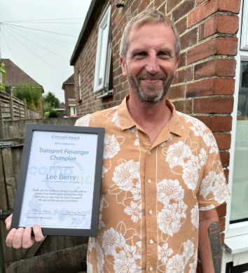 A photo of Lee, smiling, wearing a floral peach coloured shirt and holding his Transport Passenger Champion award
