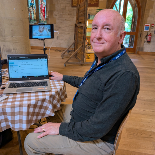Picture of digital skills trainer Norman sat at a table with a laptop beside him, in Outreach community hub at St Stephens Church in Tonbridge